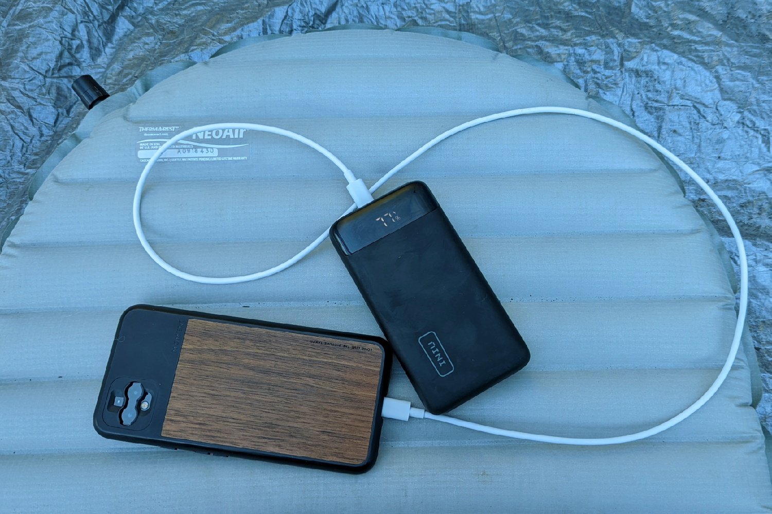 A phone plugged into the Iniu 20000 PD power bank with a phone next to it on top of a sleeping pad
