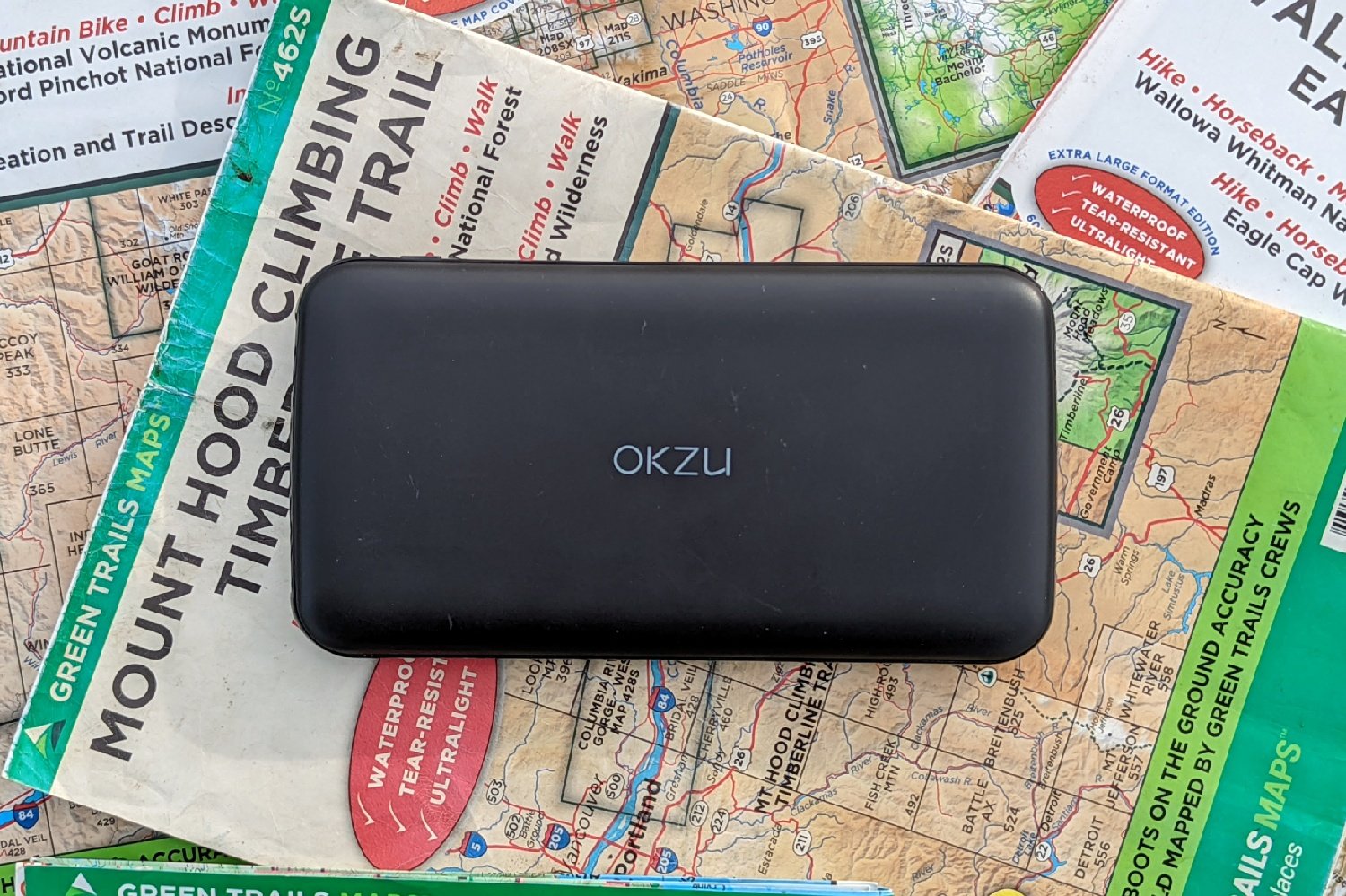 An OKZO 10000 mAh power bank sitting on a pile of hiking maps
