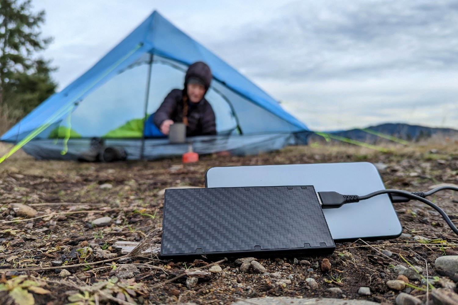 A close up of the Nitecore NB10000 with a phone plugged in - there's a hiker leaning out of a tent in the background