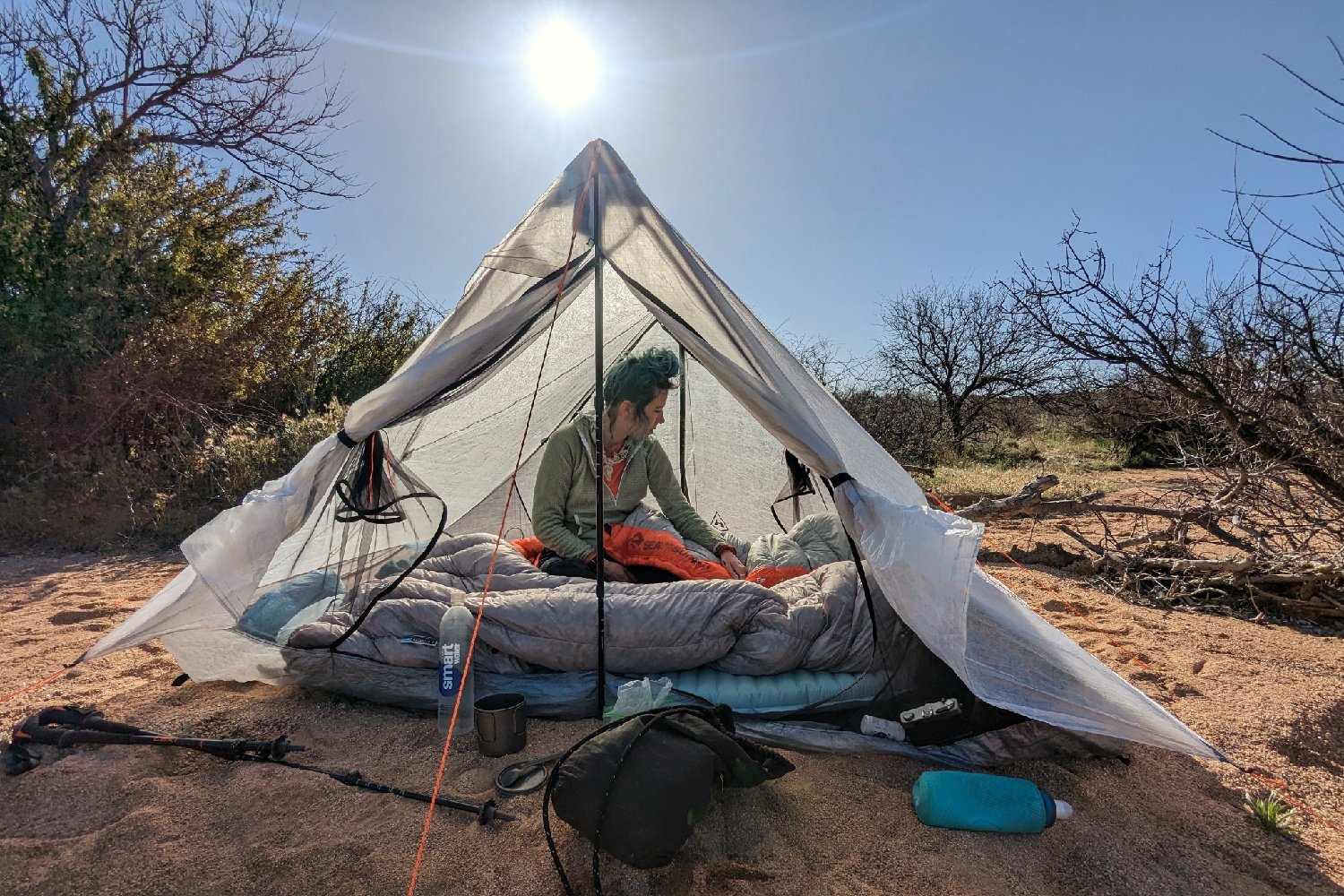 A hiker sitting in a sleeping bag inside the Hyperlite Mountain Gear Unbound 2 tent with the vestibule doors open and the sun shining brightly behind it