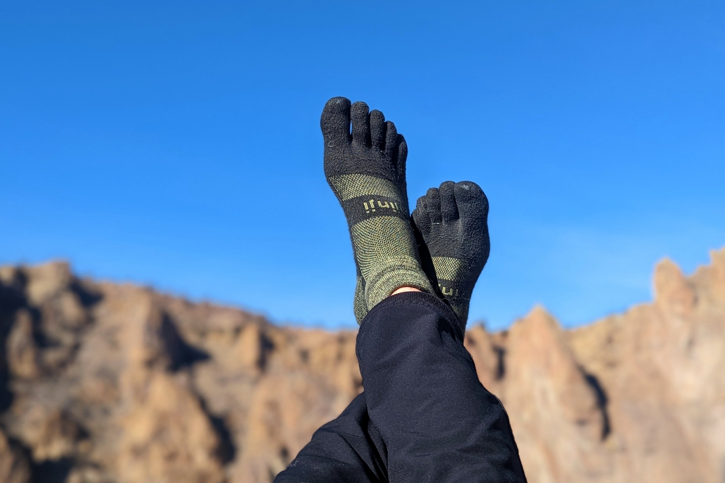 A hikers feet with Injinji socks on against a blue sky with mountains in the background