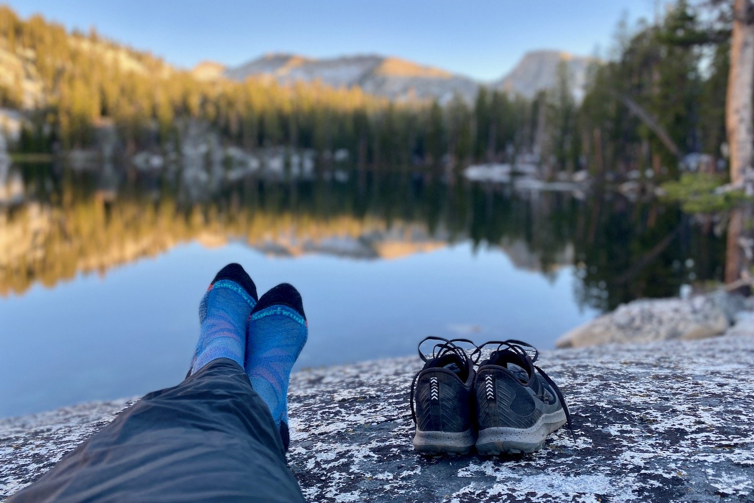 A backpacker's feet in front of a lake in the Smartwool Performance Hike Socks
